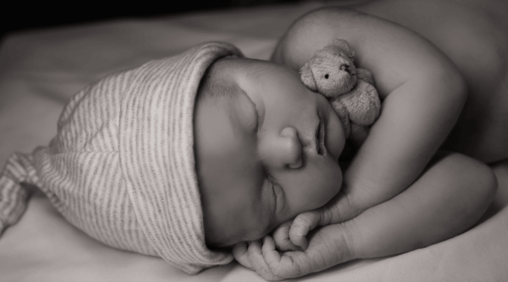 stillborn infant sleeping with a cap and holding a teddy bear