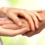 A caregiver's hands gently hold the hand of a patient