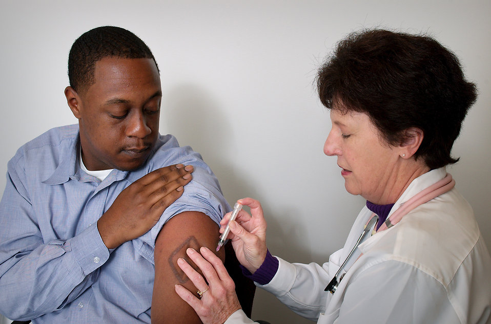 A black patient receives a shot in a hospital from a medical professional