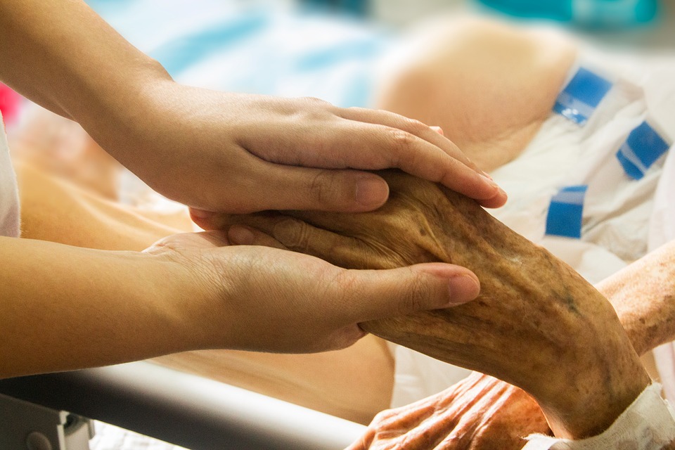 A hospice caretaker holds a patient's hand
