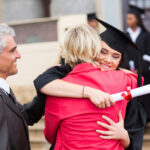 Happy young woman hugging parents at graduation despite student loan dent
