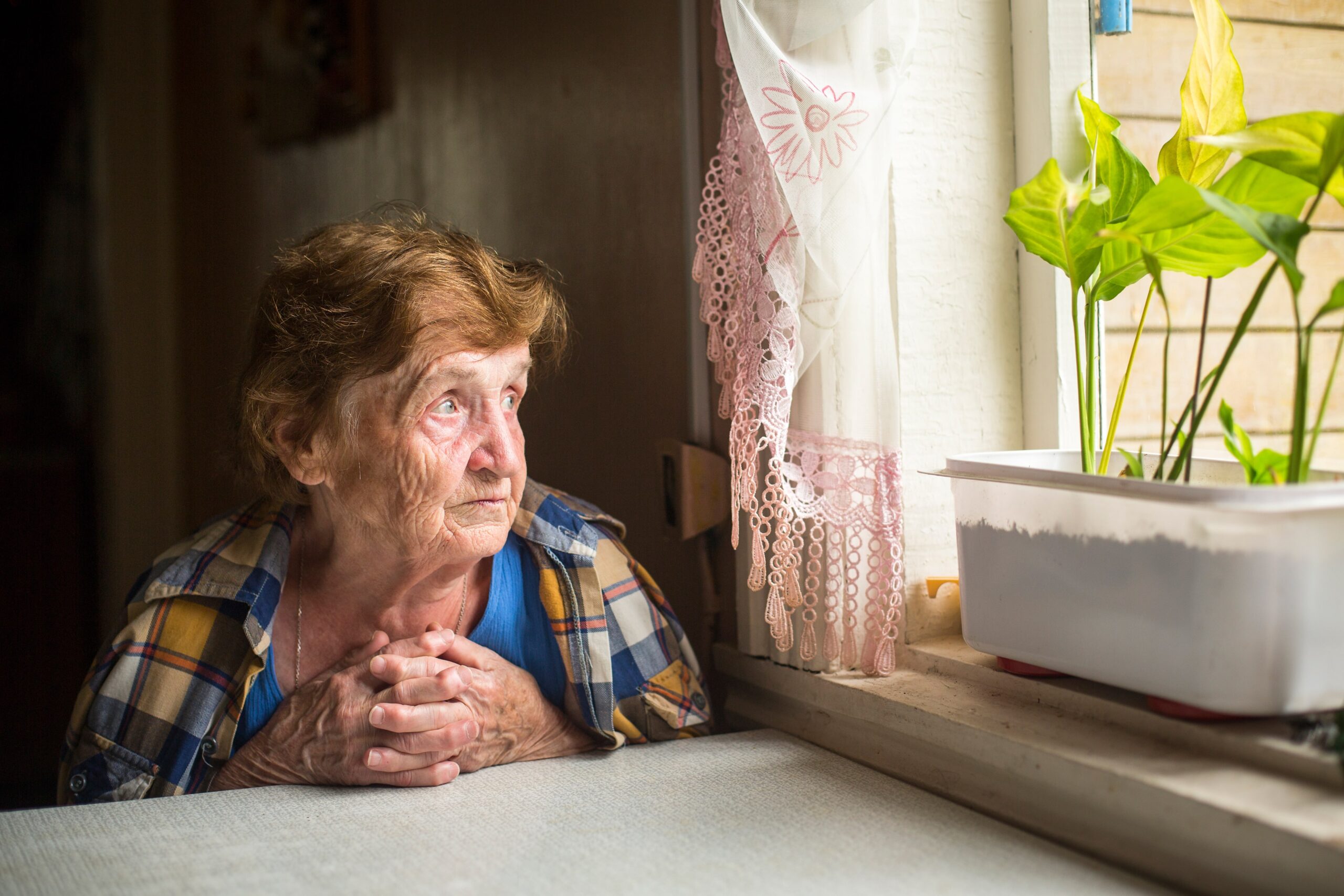 an elderly woman looking out the window experiencing loneliness