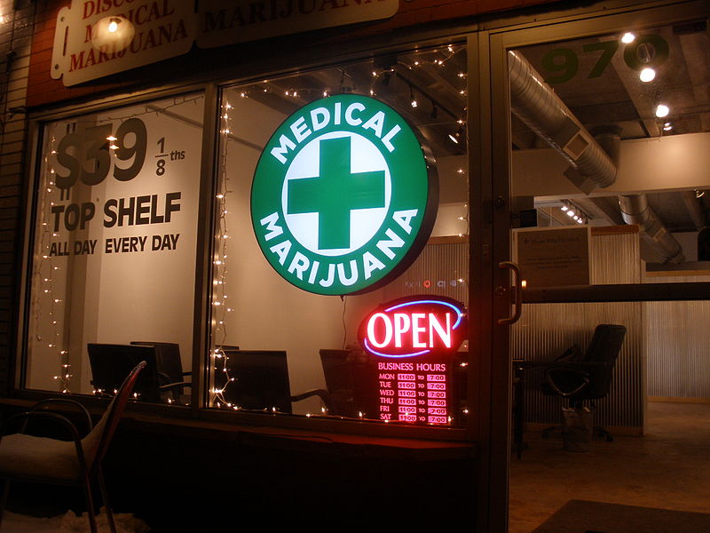 A medical marijuana building with a green sign and a medical cross at the center