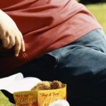 Person with obesity sitting on a park bench next to a package of chicken nuggets