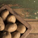 Uncooked potatoes inside of a brown wooden box
