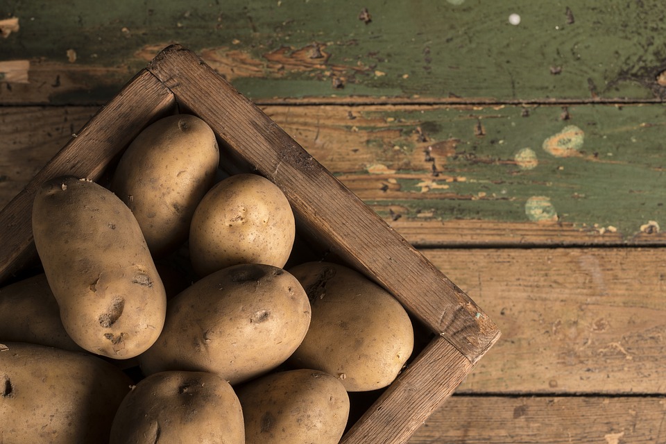 Uncooked potatoes inside of a brown wooden box