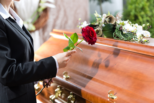 Someone holds a rose up to a coffin as part of a memorial service