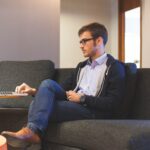 Man sitting on a couch with laptop indicating sedentary behavior.
