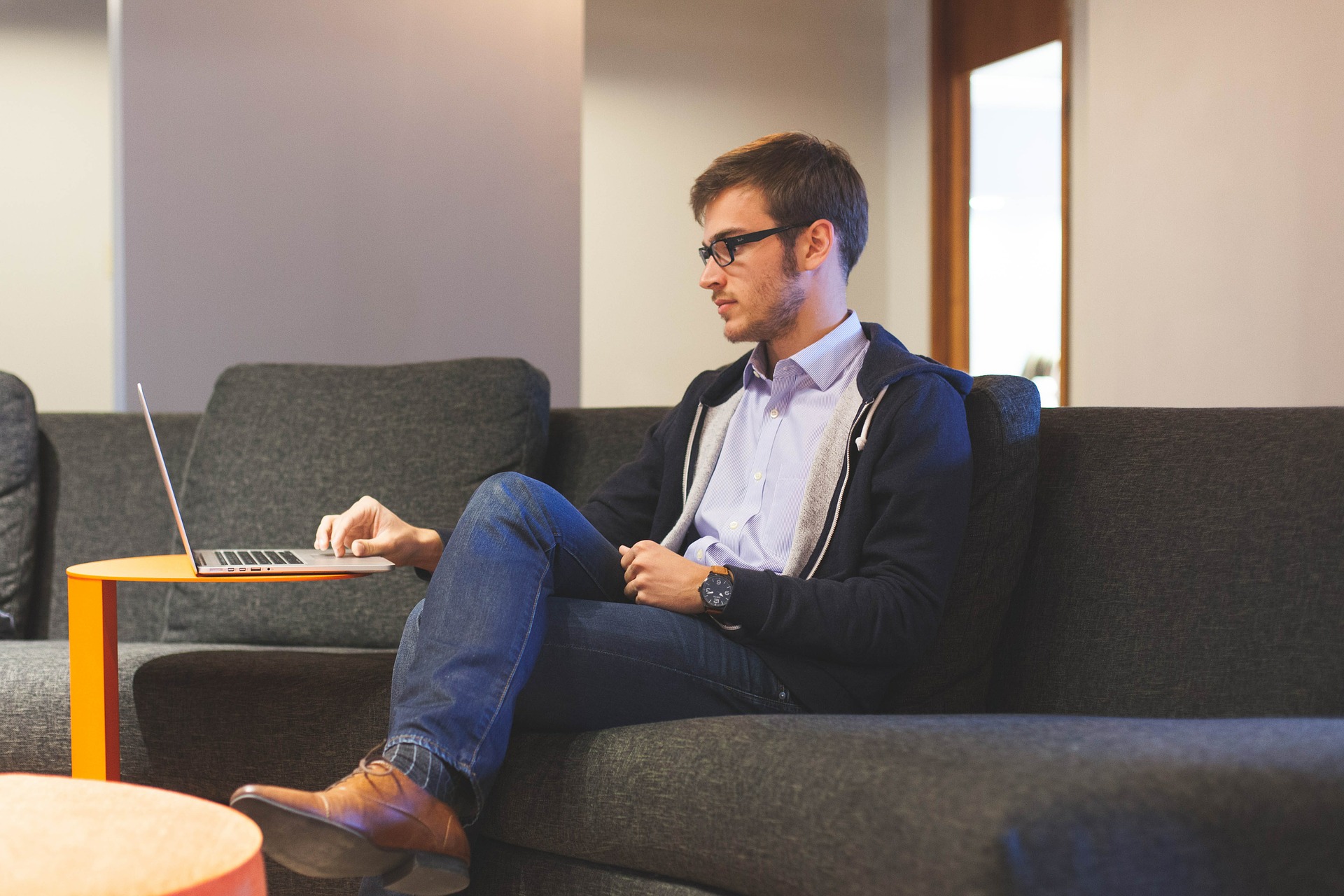 Man sitting on a couch with laptop indicating sedentary behavior.