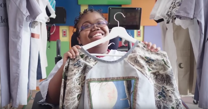 A young girl holds up her new hospital gown redesign, which features an illustration of a bird and other intricate details