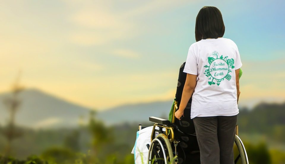 A hospice care nurse pushes a patient in a wheelchair outside