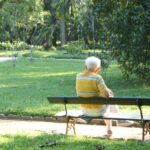 Elderly man sitting alone on park bench symbolizing aging and loneliness.