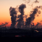 Factory smoke stacks emitting smoke at dusk.