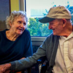 Gloria Single sits next to her husband, Bill Single in a nursing home; AARP Foundation is suing the home for illegal nursing home evictions