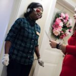 Participant in the virtual dementia tour standing with her back to a wall while a trainer reads instructions off a notecard.