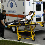 Two paramedics carry a man on a stretcher toward an ambulance