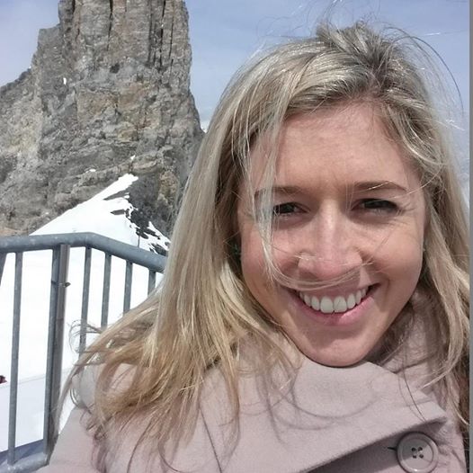 Selfie of Holly Butcher wearing a coat standing in front of a rocky pillar with snow on the ground.