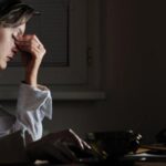 Woman clenching nose appearing tired while on computer.