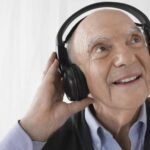 Elderly man listening to music via headphones and smiling.