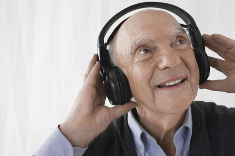 Elderly man listening to music via headphones and smiling.