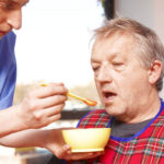 Man with late-stage dementia being fed by caregiver