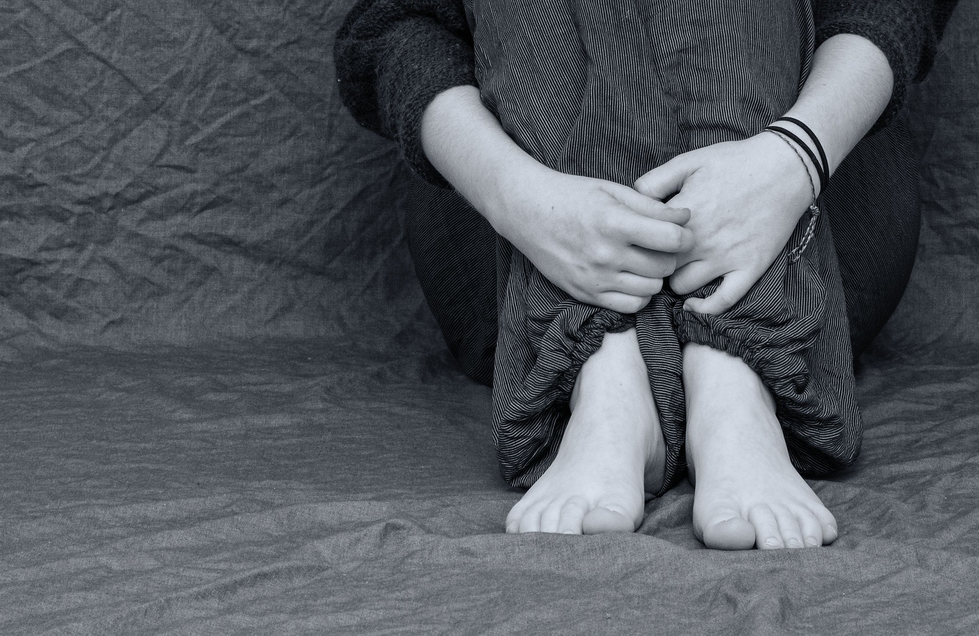 Black and white photo of a person sitting down and grasping their ankles symbolizing a state of bereavement.