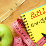 Apple, glasses, tape measure and a notebook that has the BMI equation.