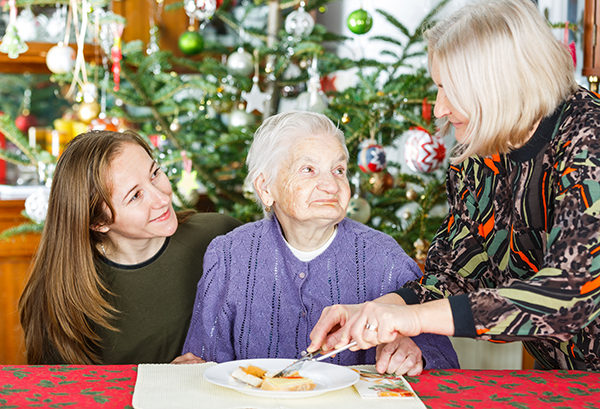 Elderly woman eating with help from caregivers.