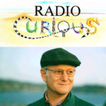Barry Vogel standing under the logo for his Radio Curious radio show.