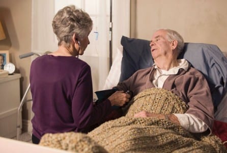 Female spousal caregiver holding her husband's hand while he lies in bed.