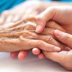 A hospice and palliative care health worker holding hands with a patient.