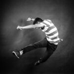 A man jumps in front of a grey background, exploring dance to cope with grief