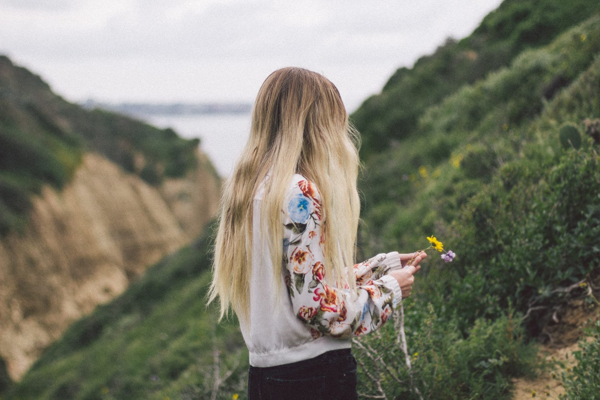 woman holds flower overlooking ocean thinking about loss