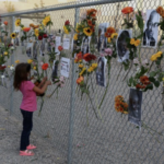 A child adds flowers to a Say Their Names Memorial with photos of victims on a fence