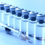 Photograph of vaccine bottles lined up next to syringe - vaccine boosters