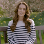Kate Middleton, the Princess of Wales, sits on a sunny park bench wearing a cream-and-black stripped sweater as she issues a statement regarding her recent surprising cancer diagnosis