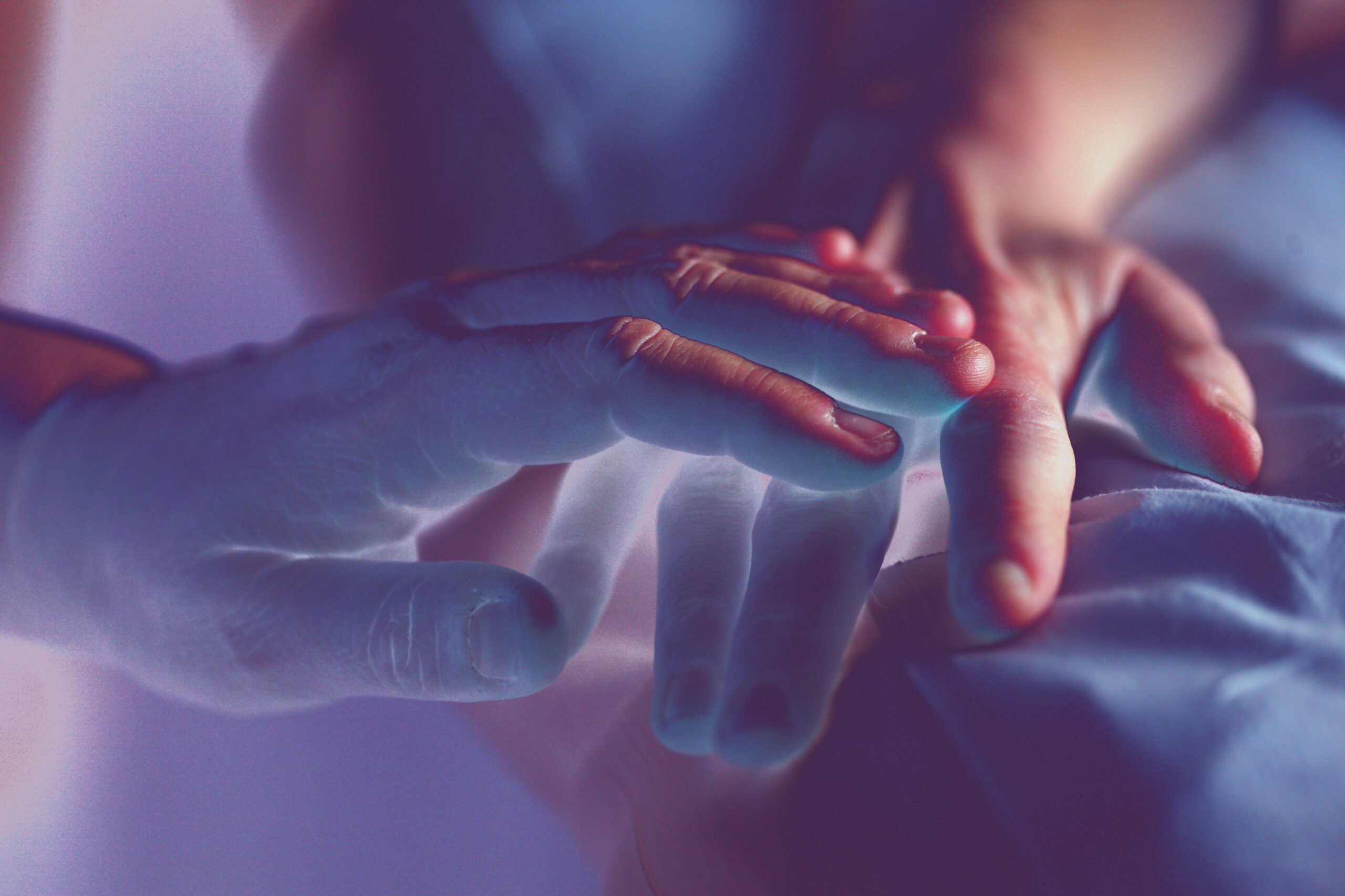 Two hands touching on a hospital bed.