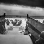 A black and white photo of soldiers storming Normandy on D-Day, from the perspective of one of the boats