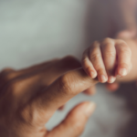 Close-up image of a tiny baby's fingers holding onto a woman's index finger