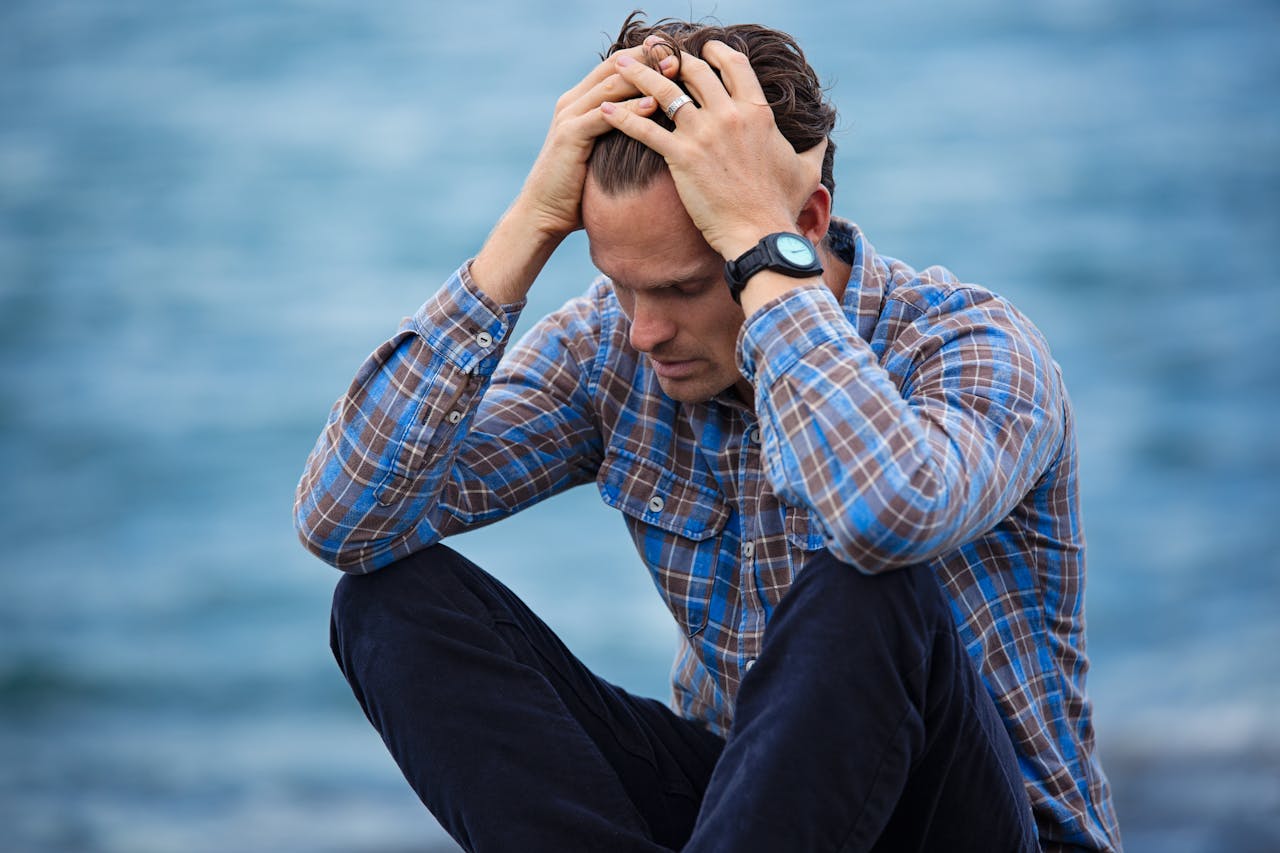Man holding head in emotional distress by a body of water.