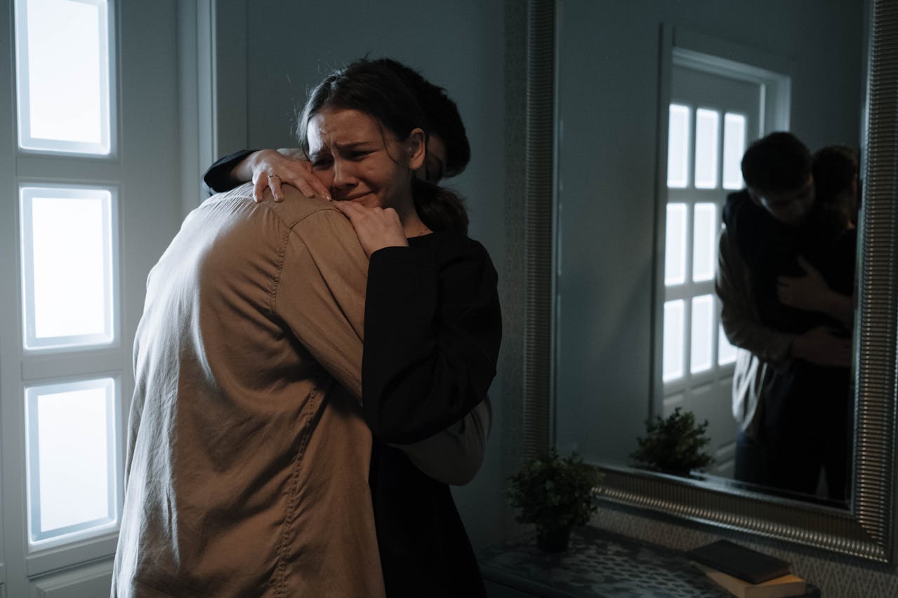 A grieving couple hugs before a mirror.