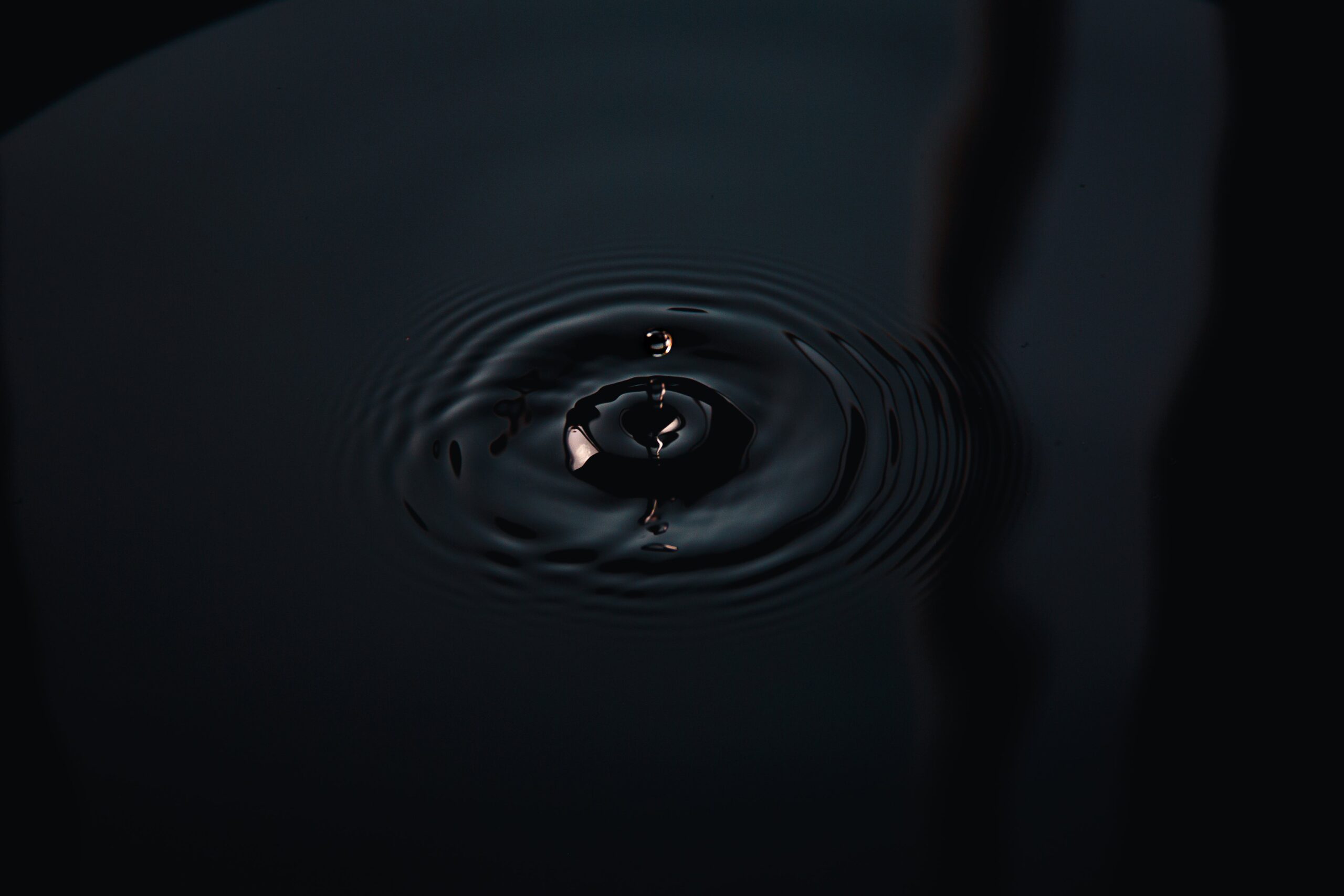 Waves spread from a drop of water hitting a black pool seen from directly overhead.