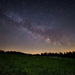 a beautiful night sky pictured above lush green grass and a glowing horizon.