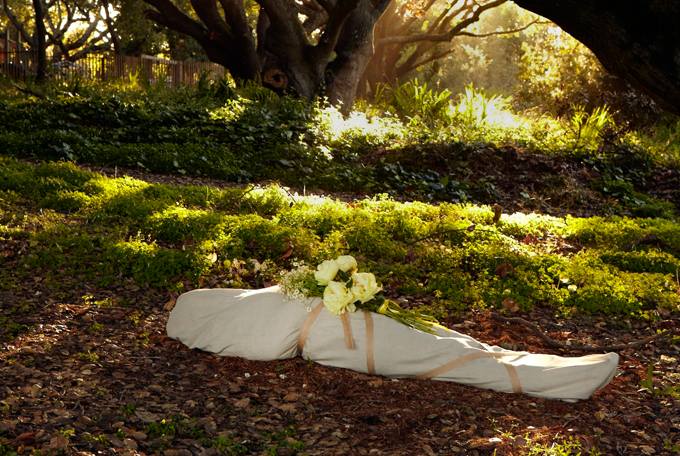 a body lays covered with flowers at a green burial