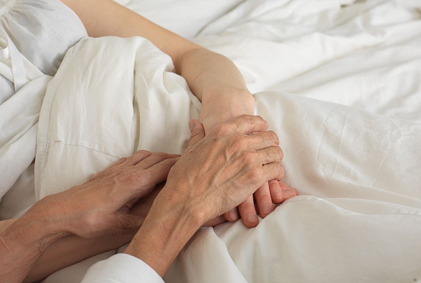 two women hold hands in an ICU bed