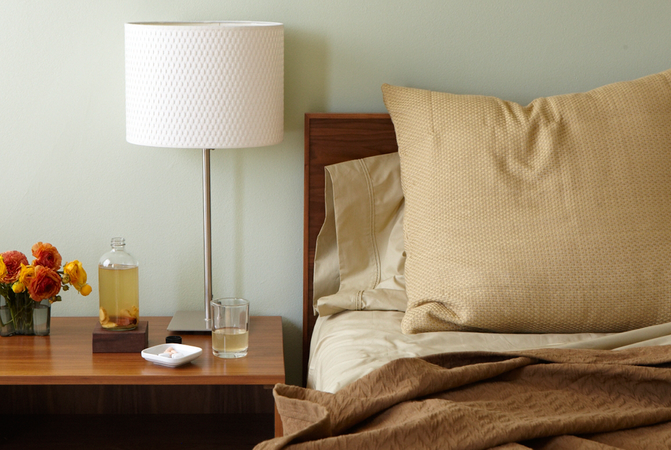 an empty bed with pills and a cup of rose water signifying medical aid in dying