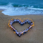 In an aerial photograph, people are formed in a heart shape on a beach and hold sparklers in their hands.