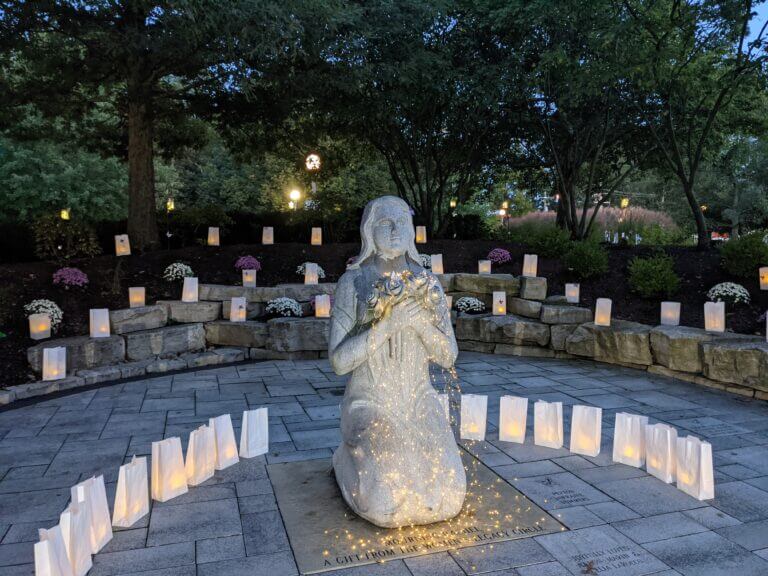 statue of angel kneeling outdoors with candle lit paperbags around in observance of infant loss