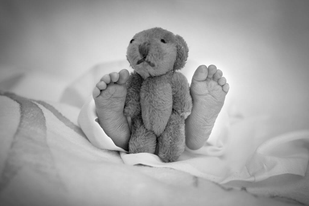 The tiny feet of an infant who died at birth with a teddy bear between her feet