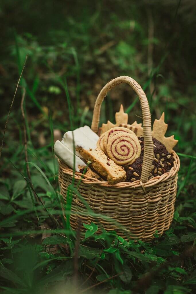 A wicker basket with freshly baked goodies like scones, cinnamon rolls, and biscotti sits in a tuft of grass at an outdoor celebration of life or memorial service.